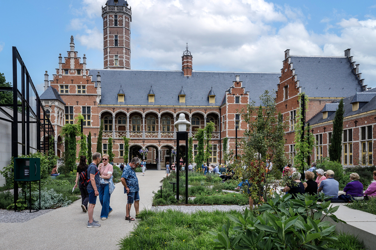 Les visiteurs se promènent dans le jardin fleuri du musée, avec la façade du palais municipal en arrière-plan.
